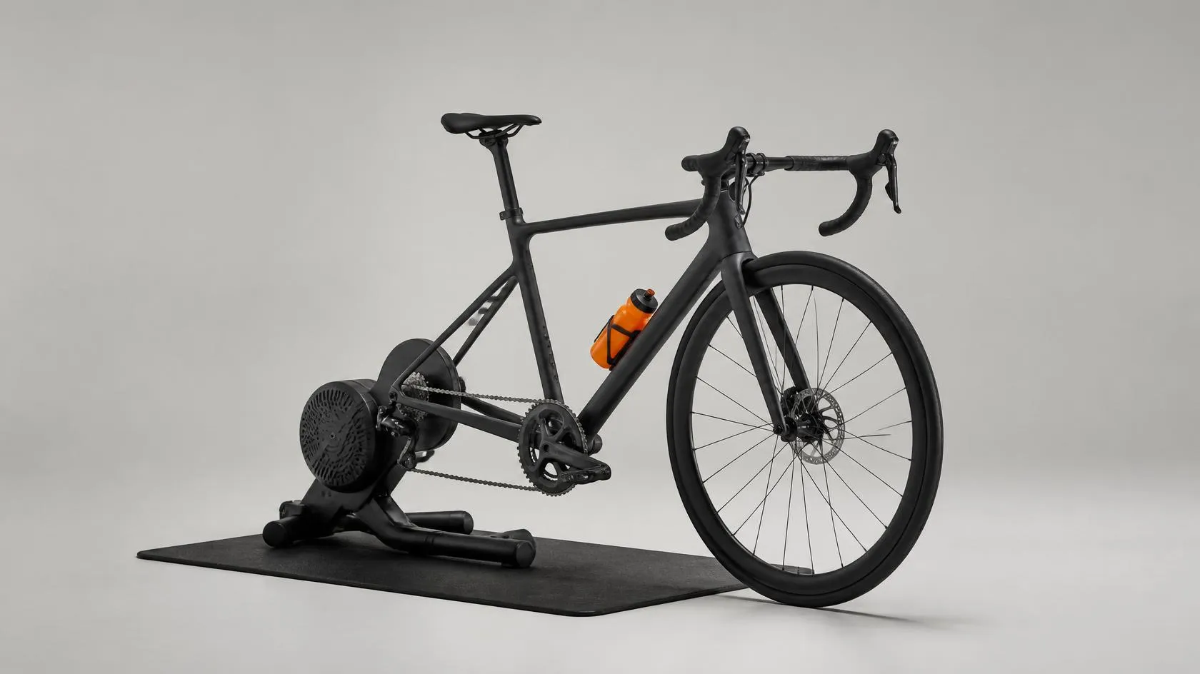 Svart racercykel monterad på en direktdriven smart trainer i ljus studio, med en orange vattenflaska i flaskhållaren
